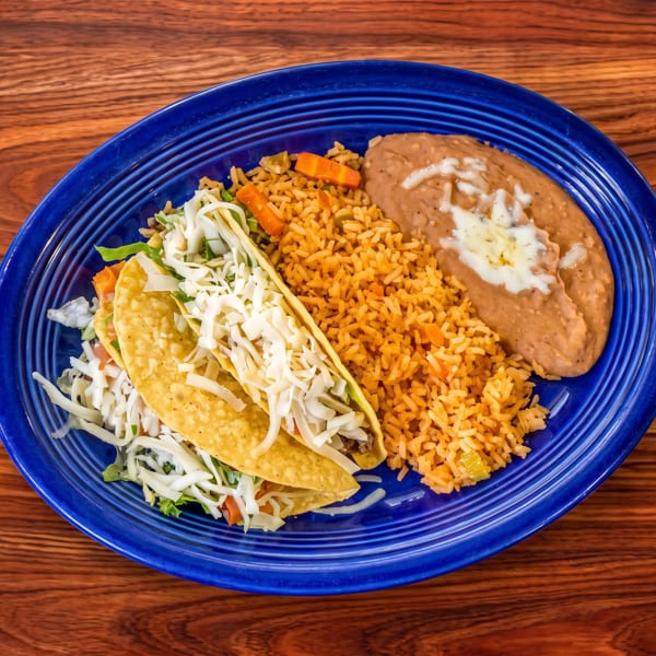 Mexican meal with two hard-shell tacos, rice, and refried beans on a blue plate.