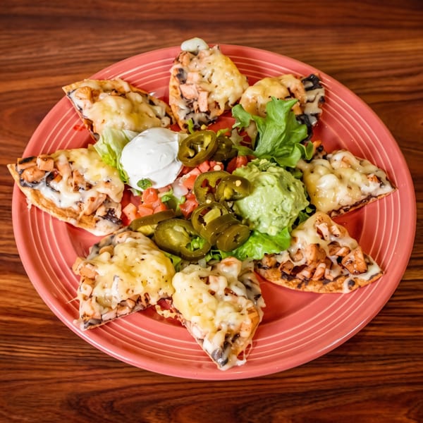 Plate of chicken nachos with melted cheese, guacamole, sour cream, pico de gallo, and jalapeños.