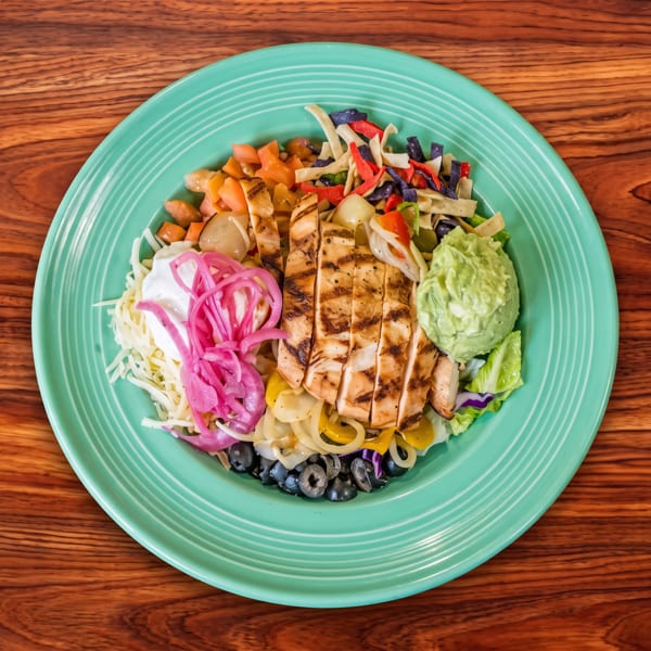 Grilled chicken salad bowl with guacamole, pickled onions, and tortilla strips on a teal plate.