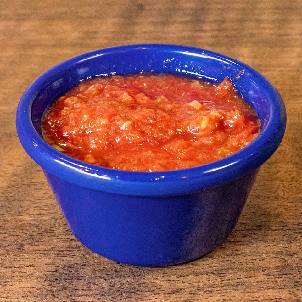 Bright red salsa in a small blue bowl on a rustic wooden table.